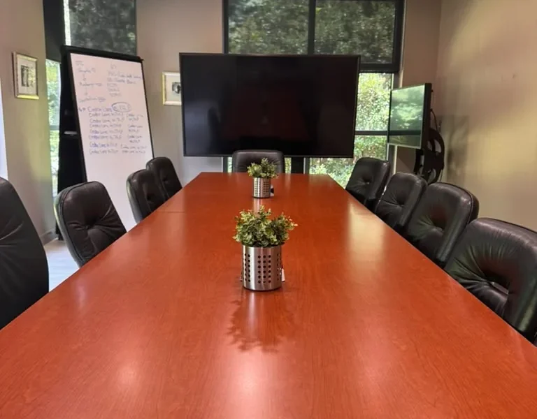 Einstein boardroom at World Park with a long wooden conference table, leather chairs, a TV and a whiteboard easel