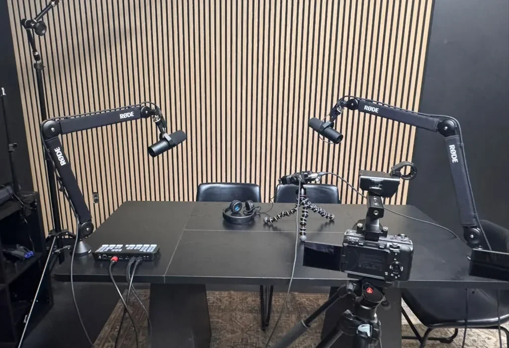 Podcast and video studio at World Park in Alpharetta with broadcast microphones on boom arms, a camera on a tripod and an acoustic wood-slat wall