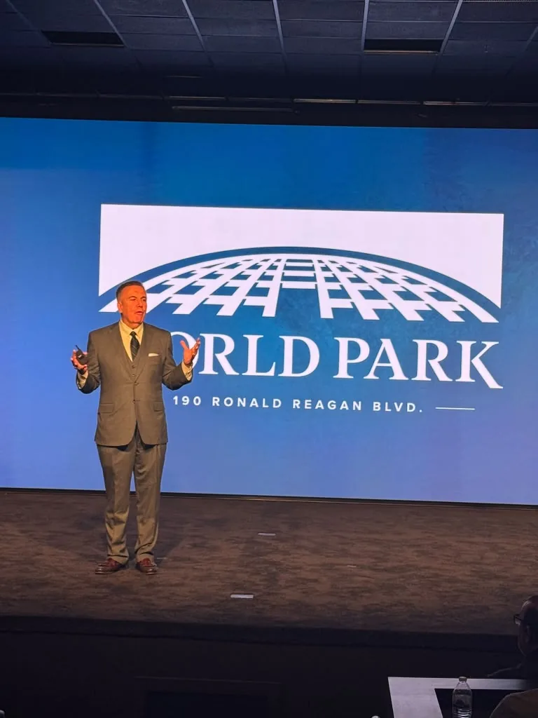 Speaker on stage in front of the World Park logo at the WealthWave grand opening
